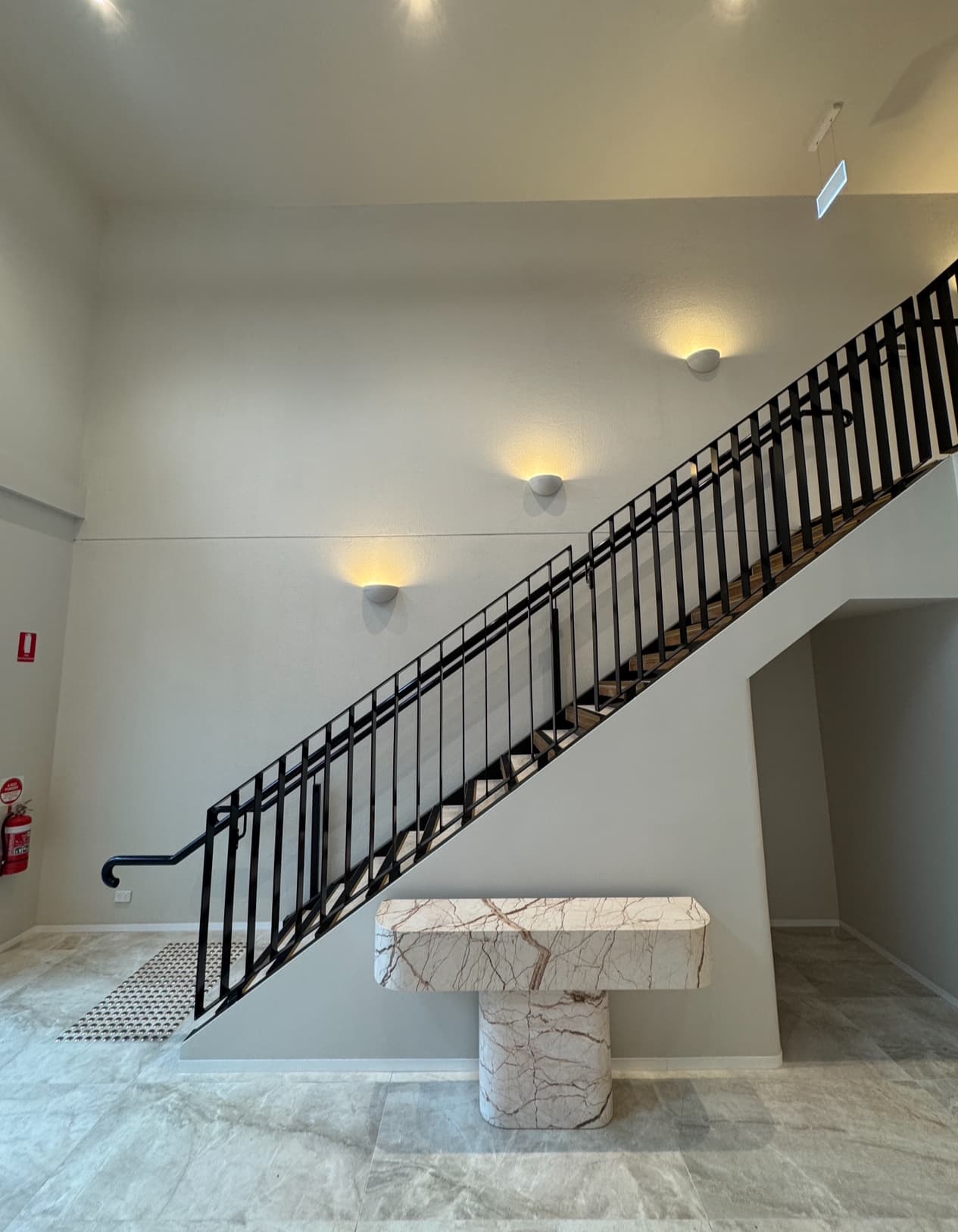 Minimalist staircase with black metal railings and a marble console table under warm wall lights.